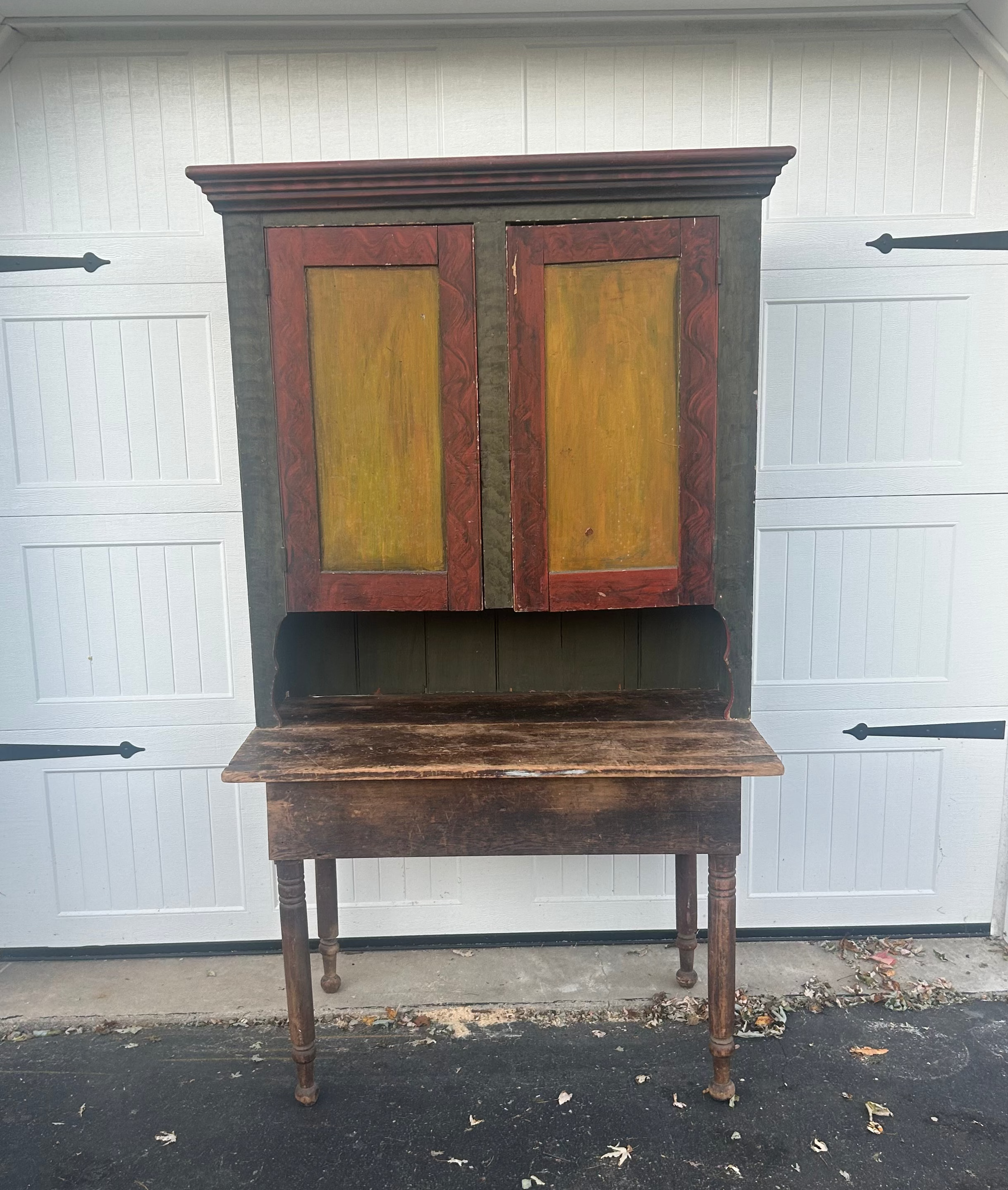 Vintage wooden cabinet with yellow doors in front of a white garage door.