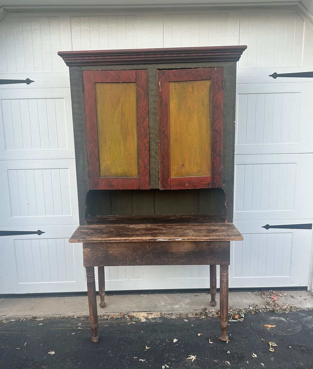Vintage wooden cabinet with yellow doors in front of a white garage door.